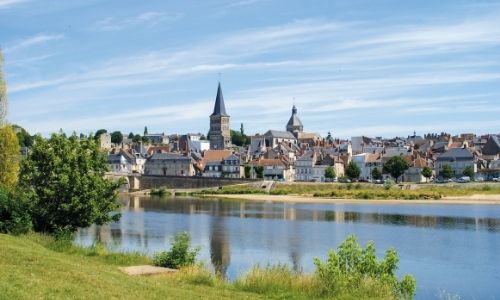 vu de loin d’une ville français avec des habitations et un grand bâtiment, au premier plan une grande étendue d’eau