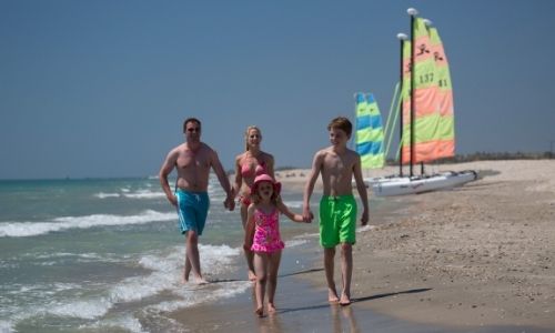 Une famille en bord de mer avec des catamarans en fond sur le sable