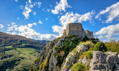 Un château Cathare moyennement conservé est perché sur une colline rocheuse.