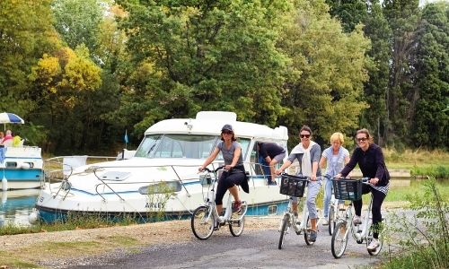 Une famille faisant du vélo sur les berges du canal du Midi avec un bateau sans permis en fond